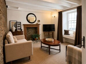 A living room with a fireplace, a television, a sofa, and a window with curtains. - Heart of St Davids Cottage| Parking | Pet Friendly (St Davids)