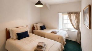 Ein Zimmer mit zwei Betten, einem Vorhangfenster, einer Hängelampe und einem gerahmten Bild an der Wand.