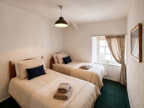 A room with two beds, a window with curtains, a hanging light fixture, and a framed picture on the wall. - Heart of St Davids Cottage| Parking | Pet Friendly (St Davids)