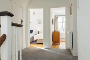 Ein Flur, der in ein Schlafzimmer mit Bett, Nachttisch und einem fenster mit Vorhängen führt.