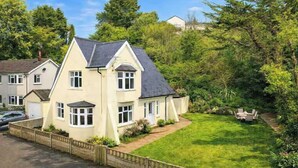Une maison à deux étages avec un toit en pente, une pelouse devant et un coin repas aménagé avec du mobilier d’extérieur.