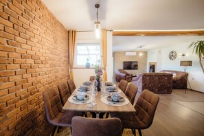 A dining area with a brick wall, a wooden table set for four, and a sofa in the background. - Vinewood - Saltwater Pool, Jacuzzi and Stunning Vineyard View (Zelezna Gora)