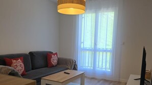 A living room with a sofa, a coffee table, a TV, and a window with curtains. - Renovated mountain studio - 4 guests (Aisa-Candanchú)