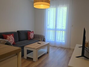 Ein Wohnzimmer mit einer Couch, einem Couchtisch, einem Fernseher und einem Fenster mit Vorhängen.