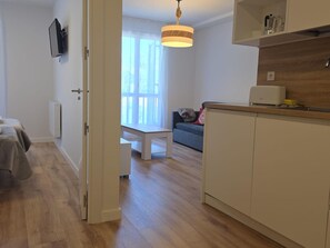 Ein modernes Apartment mit Holzboden, Essbereich, Sofa, Wand-Fernseher und Küchenzeile.