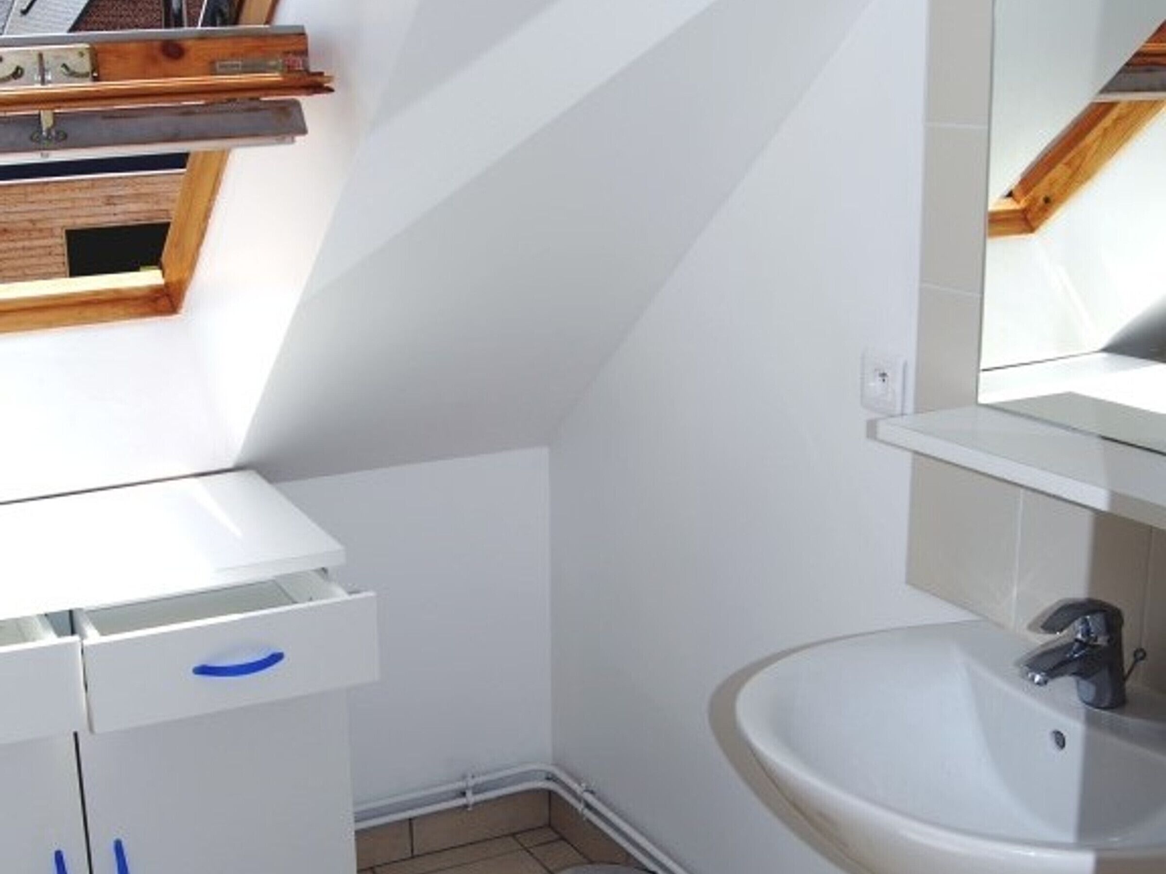 Une salle de bain avec un lavabo blanc, un miroir et une étagère en bois au-dessus du lavabo.