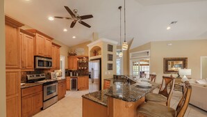 A spacious kitchen with wooden cabinets, a central island, and a ceiling fan. - Great Location! Close to library, 3 bed - 2bath and pool (Cape Coral)