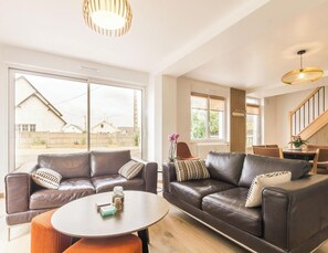 Ein modernes Wohnzimmer mit Ledersofas, einem runden Couchtisch und großen Fenstern mit Blick ins Freie.