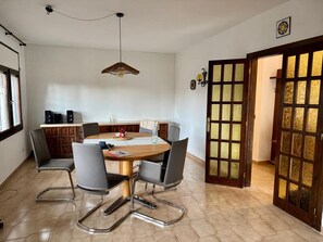 Een eetruimte met een ronde tafel, zes stoelen, een hanglamp, een houten kast en een decoratieve deur met glaspanelen.