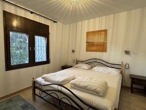 Ein Schlafzimmer mit Bett, Fenster, Nachttisch und Wandleuchte.