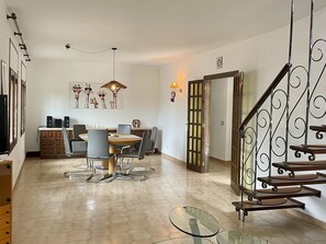 A spacious living area with a dining table, chairs, a glass coffee table, a staircase with a metal railing, and a wall-mounted light fixture. - Villa with private pool and air conditioning - 8 guests (Miami Playa)