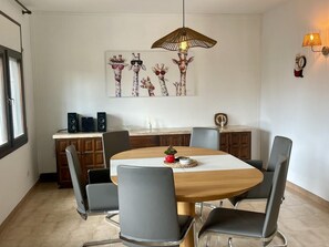 A dining area with a round table, grey chairs, a wooden cabinet, a decorative wall piece, and a hanging light fixture. - Villa with private pool and air conditioning - 8 guests (Miami Playa)