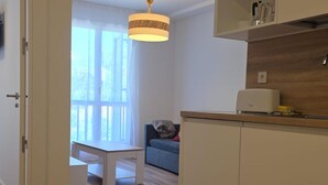 Una cocina moderna con armarios blancos, un comedor con mesa y sillas blancas, y una ventana con cortinas traslúcidas.