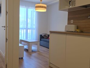 Eine moderne Küche mit weißen Schränken, ein Essbereich mit weißem Tisch und Stühlen sowie ein Fenster mit transparenten Vorhängen.