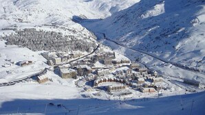 Une ville de montagne enneigée, avec des pistes de ski, des bâtiments et un ciel dégagé.