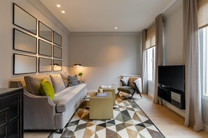 Ein modernes Wohnzimmer mit Sofa, Sessel, Couchtisch und Fernseher.