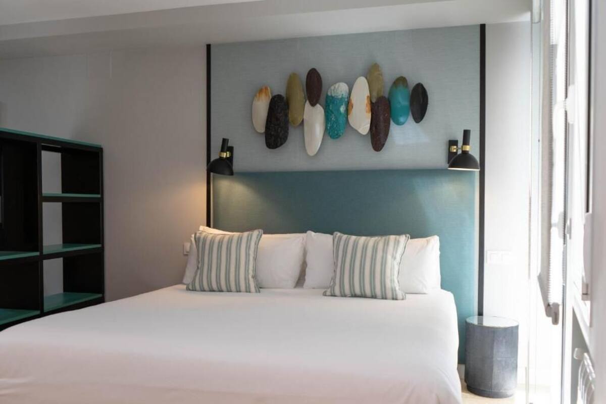 A bed with white bedding, striped pillows, and a wall-mounted light fixture.