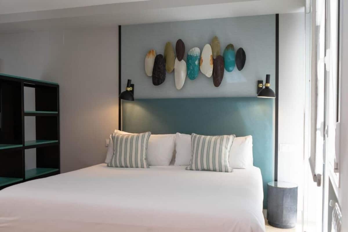 Una cama con ropa de cama blanca, almohadas a rayas y una lámpara de pared.