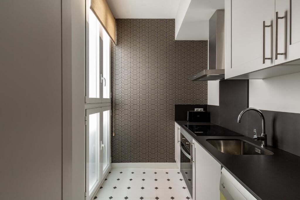 Una cocina compacta con encimera negra, pileta de acero inoxidable y un salpicadero con diseño.