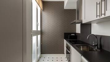 Una cocina compacta con encimera negra, pileta de acero inoxidable y un salpicadero con diseño.