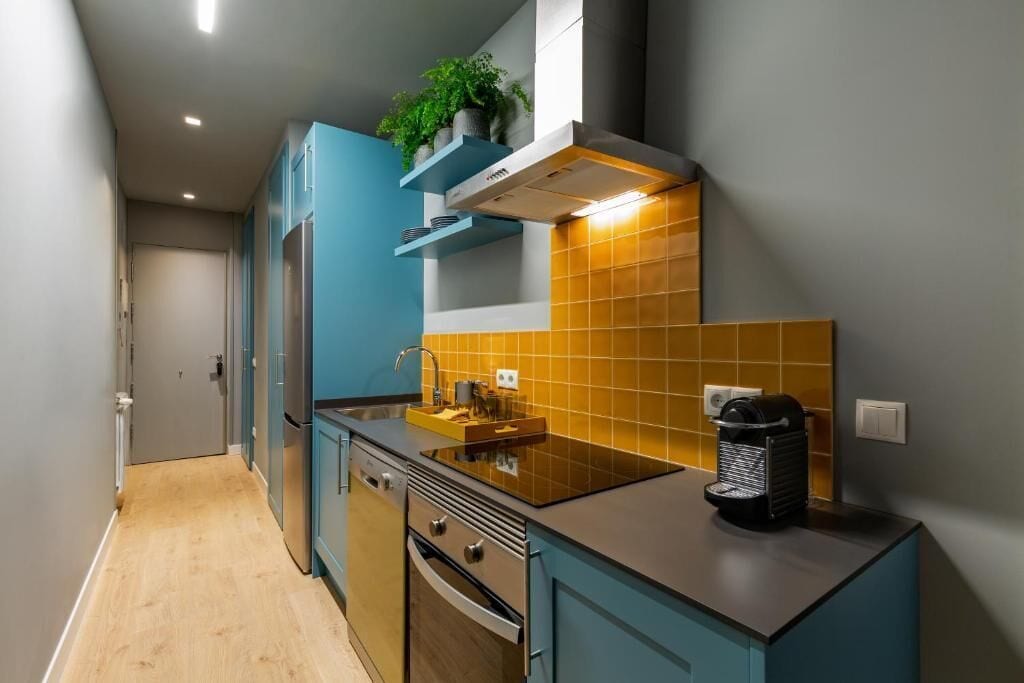 A modern kitchen with teal cabinets, a black countertop, and a yellow-tiled backsplash.