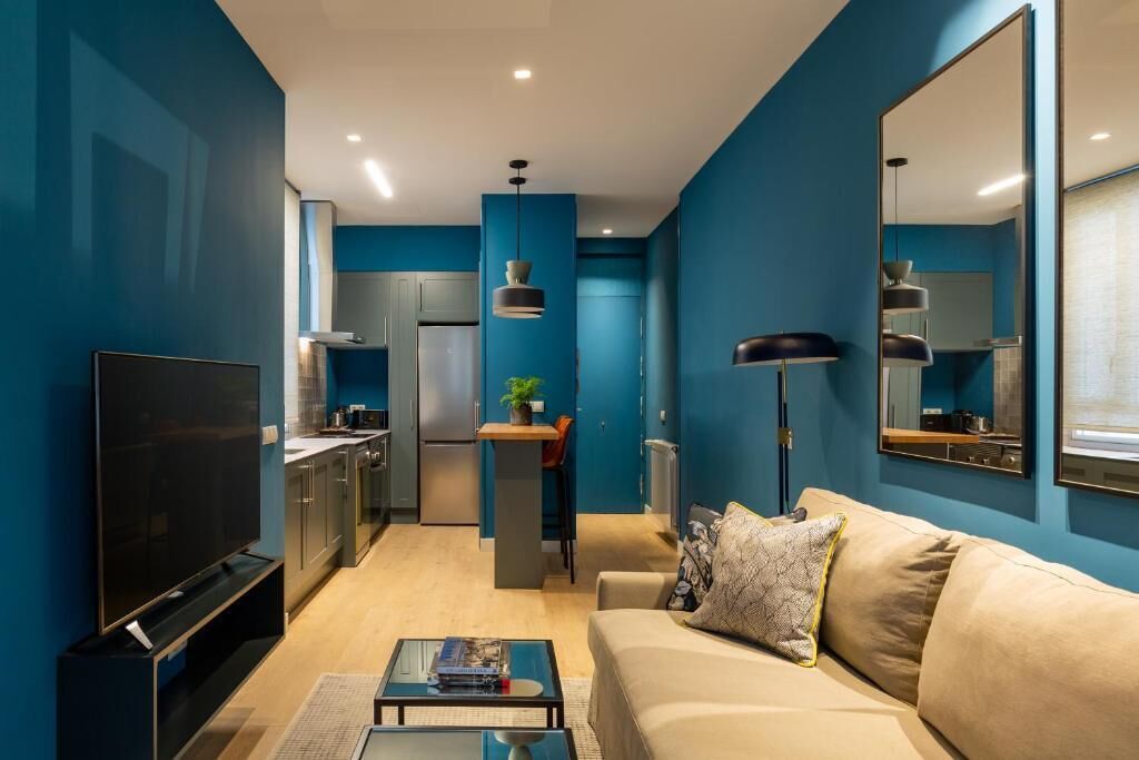 Un salon moderne comprenant un canapé, une table basse, un téléviseur et un coin cuisine avec des placards et des appareils électroménagers.