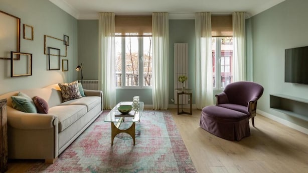 Ein Wohnzimmer mit Sofa, Sessel, Couchtisch und einem Fernseher an der Wand.