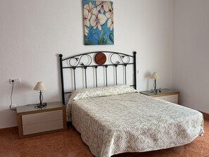 Quarto com uma cama, duas mesas de cabeceira, uma luminária, um quadro e uma tomada.