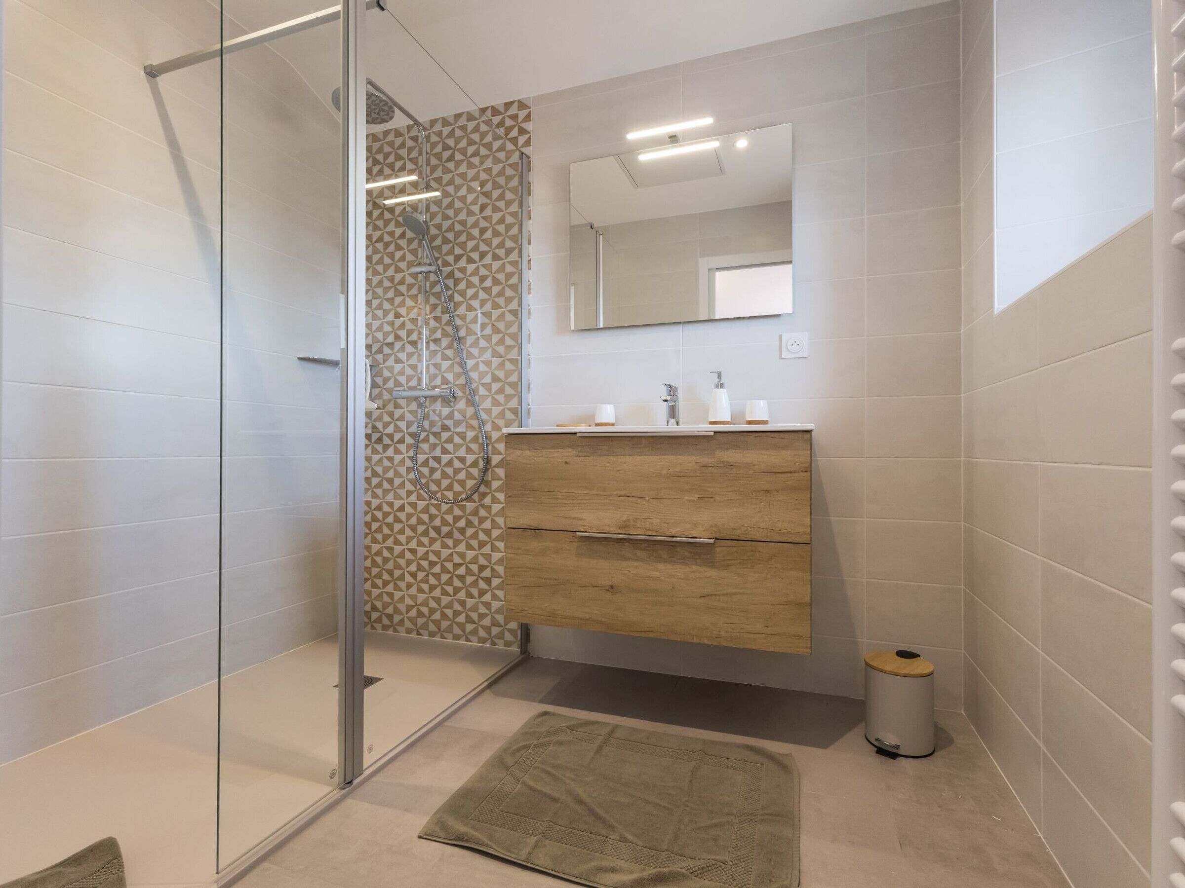 Une salle de bain moderne avec une douche à parois de verre, un meuble-lavabo en bois et un sol carrelé.