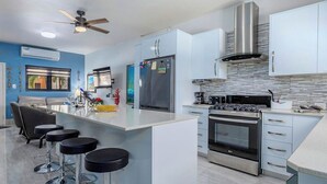 Una cucina moderna con isola centrale, sgabelli da bar, elettrodomestici in acciaio inossidabile e una ventola a soffitto.