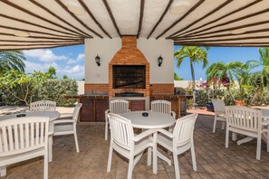 Eine Terrasse im Freien mit Kamin aus Ziegeln, weißen Stühlen und einem runden Tisch.