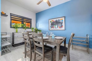 Ein Essbereich mit einem für vier Personen gedeckten Tisch, Stühlen, einem Deckenventilator und einer blauen Wand mit einem gerahmten Bild.