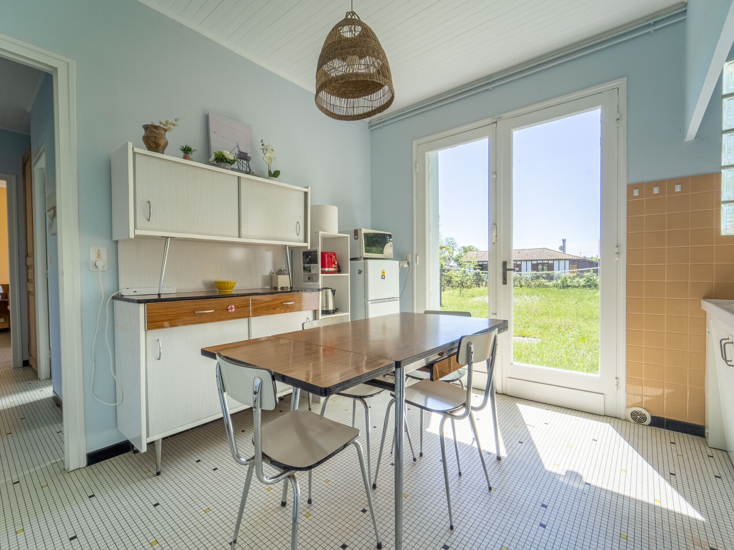 A kitchen with a dining table, chairs, a hanging light fixture, and a view through a glass door.