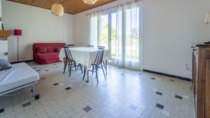 Una habitació amb sostre de fusta, taula de dinar amb cadires, un sofà vermell i un llit.