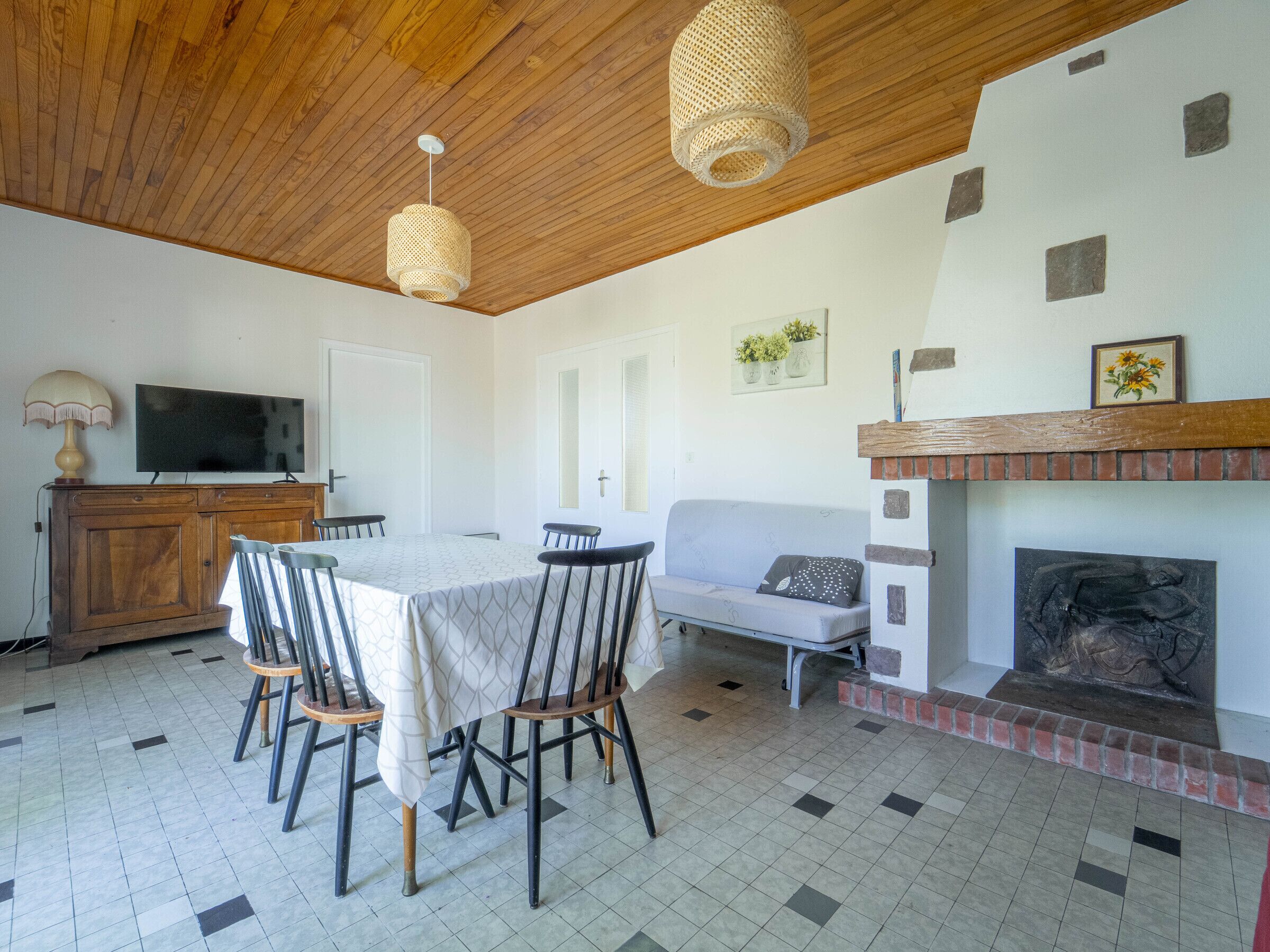 Un área de comedor con una mesa y sillas, un televisor sobre un mueble de madera, un sofá y una chimenea.