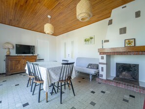 Ein Essbereich mit Tisch und Stühlen, einem Fernseher auf einer Holzkassette, einer Couch und einem Kamin.