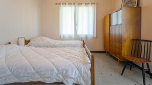 Un dormitori amb dos llits, un armari de fusta, una cadira i una finestra amb cortines.