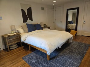 Une chambre à coucher avec un lit, des tables de chevet, un miroir et une porte.