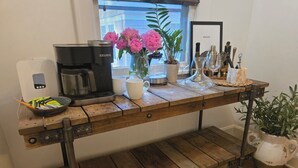 A wooden coffee table with a Keurig coffee maker, a mug, a vase with flowers, and a framed picture on a wall. - Walk to Brookside, Shops/Dining, 3BR, patio, backyard bar.   9 miles 2 World Cup (Kansas City)