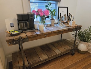 Ein Holztisch mit einer Keurig-Kaffeemaschine, einer Tasse, einer Vase mit Blumen und einem gerahmten Bild an der Wand.