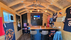 A bar area with wooden beams, a TV screen, sports jerseys, and stools. - Walk to Brookside, Shops/Dining, 3BR, patio, backyard bar.   9 miles 2 World Cup (Kansas City)