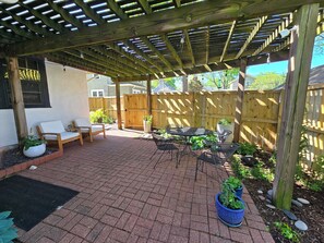 A covered patio area with a wooden pergola, outdoor seating, and potted plants. - Walk to Brookside, Shops/Dining, 3BR, patio, backyard bar.   9 miles 2 World Cup (Kansas City)