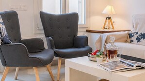 Un salón moderno con dos sillones tapizados de gris, una mesa de centro blanca, una lámpara y un cojín con un mapa mundial en un sofá.