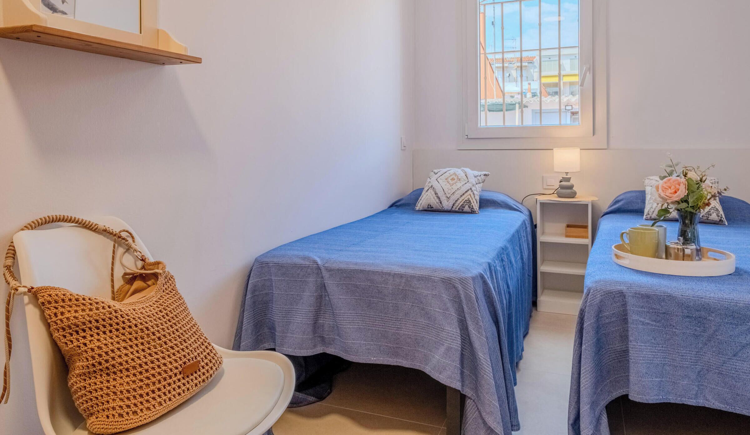 A room with two beds, a chair, a small table with a lamp, and a window.