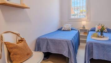 A room with two beds, a chair, a small table with a lamp, and a window.