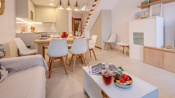 Una sala de estar moderna con comedor, una cocina al fondo y una escalera que sube a un nivel superior.