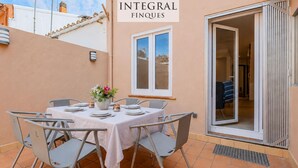 Un patio con una mesa lista para cuatro, un florero con flores y una puerta corrediza de vidrio que da a un espacio interior.