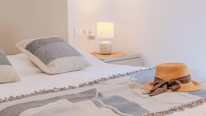 Una cama bien tendida con una colcha estampada, una almohada decorativa y un sombrero tejido al lado.