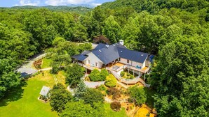 A large house with a spacious deck, surrounded by dense forest.