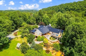 Una casa grande con una amplia terraza, rodeada de un bosque frondoso.